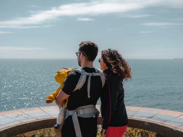 Young parents and their baby admiring the horizon from the orientation table at Pointe de Groasguen