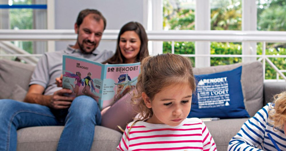 Couple lisant la brochure de Bénodet assis sur un canapé