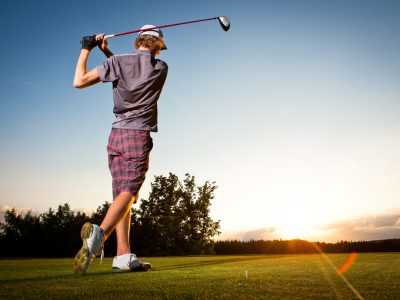 Männlicher Golfspieler, der Golfball vom Teekasten zum schönen Sonnenuntergang abschlägt