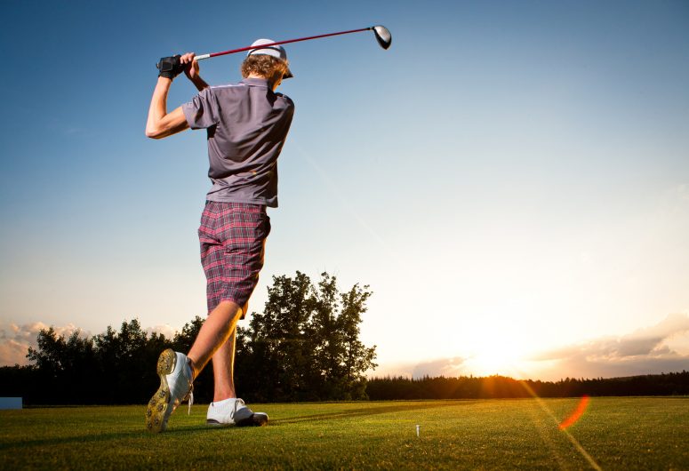 Male golf player teeing off golf ball from tee box to beautiful sunset